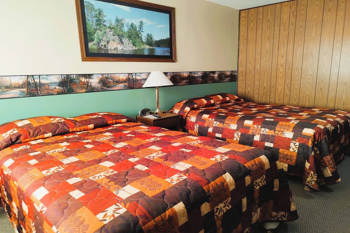 Ein Hotelzimmer mit zwei Betten, einem Gemälde einer Seelandschaft, einem Holzkopfteil und einer Lampe.
