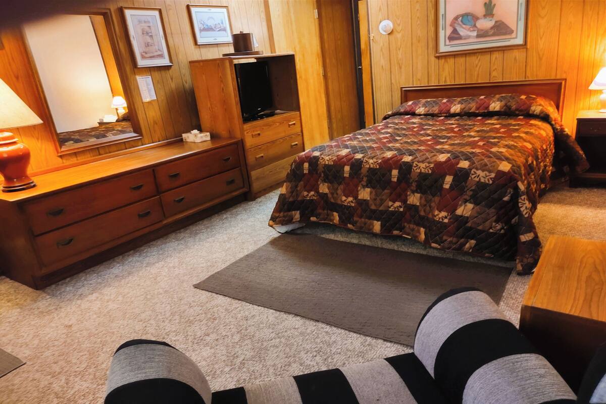 Ein Schlafzimmer mit Bett, Holzkommode und Fernseher.