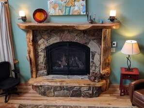 A stone fireplace with a wooden mantel, a framed painting above it, and a small table with a lamp beside it. - Gorgeous five bedroom home sleeps up to 13 guests. Extensive decks wrap the home, fishing pond, 11 acres with forest, pasture, and abuindance of wildlife. (Ashford)