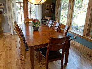 A wooden dining table with six chairs, a potted plant, and a window with a view of greenery. - Gorgeous five bedroom home sleeps up to 13 guests. Extensive decks wrap the home, fishing pond, 11 acres with forest, pasture, and abuindance of wildlife. (Ashford)