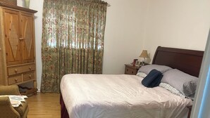 A bedroom with a bed, a wooden wardrobe, a nightstand, a lamp, and a floral curtain.