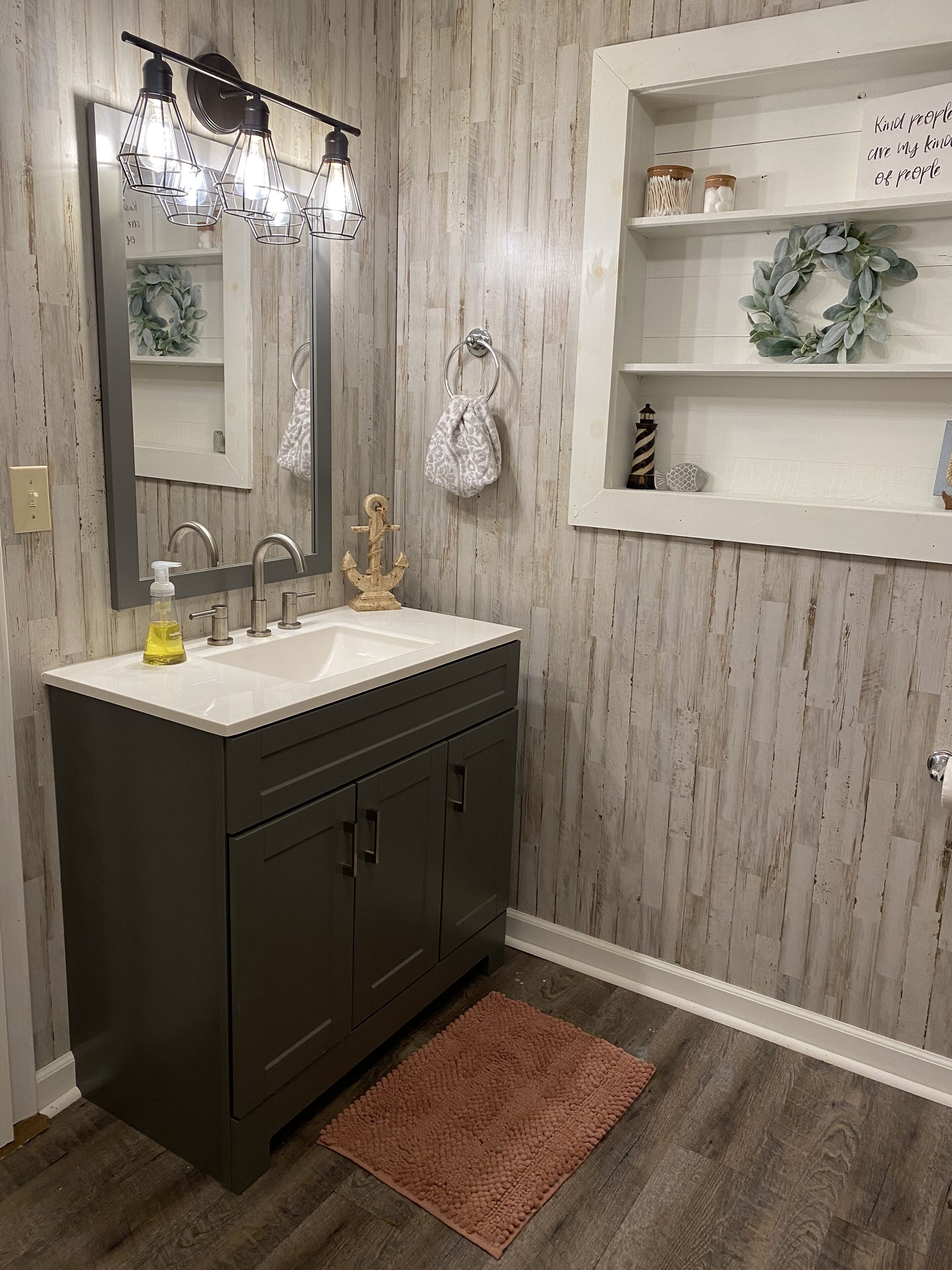 A bathroom with a dark vanity, a mirror, a sink with a soap dispenser, and a wooden floor.