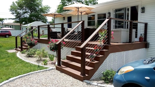 Une maison avec un escalier en bois menant à un porche couvert où se trouvent deux parasols.