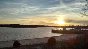 Un coucher de soleil sur une étendue d’eau calme, avec une jetée qui s’avance dans l’eau, le tout entouré d’une végétation clairsemée et d’une côte lointaine.