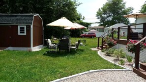 Ein Garten mit einer Terrasseneinrichtung, einem Grill und einem überdachten Bereich mit Sonnenschirm.
