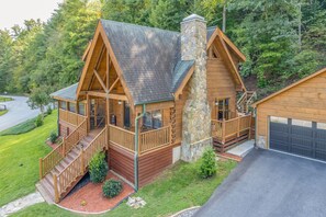 Une cabane en rondins avec une cheminée en pierre, une véranda et un garage.