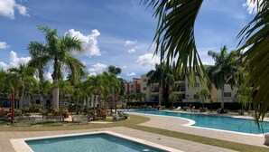 A swimming pool area with multiple pools, palm trees, and a building in the background.