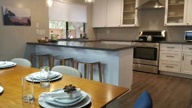 A modern kitchen with white cabinets, stainless steel appliances, and a wooden dining table set for four. - Hiker's Haven - The Start of a Beautiful, Adventurous and Peaceful Vacation (Sedona)