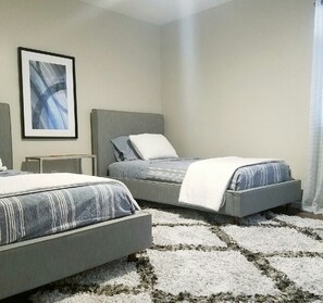 A bedroom with two beds, a framed abstract painting, a bedside table, and a patterned rug.
