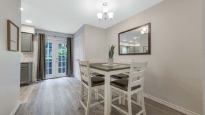Een eetgedeelte met een tafel, stoelen, een potplant en een spiegel aan de muur.