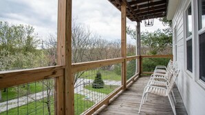 Une terrasse en bois avec une rambarde, des chaises blanches et une vue sur les arbres et une pelouse.