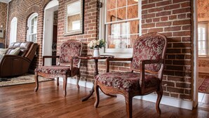 Une pièce avec un mur en briques, deux fauteuils décoratifs recouverts d’un tissu à motifs floraux, un fauteuil de massage et une petite table sur laquelle est posé un vase de fleurs.