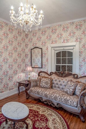 Habitación de estilo vintage con papel tapiz floral, un sofá capitonado, una araña y una mesa de mármol.