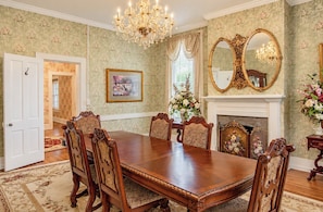 A formal dining room with a large wooden table, ornate chairs, a chandelier, and floral wallpaper. - The Manor 1885 Altamont (Altamont)
