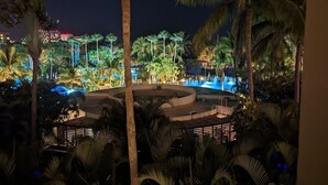 Une vue nocturne d’un complexe hôtelier avec une piscine circulaire, entourée de palmiers et illuminée de lumières bleues.