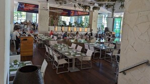 Un restaurant spacieux avec de hauts plafonds, des plantes suspendues et un bar central.