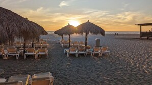 Une plage avec des parasols en chaume et des chaises longues disposées pour prendre des bains de soleil.