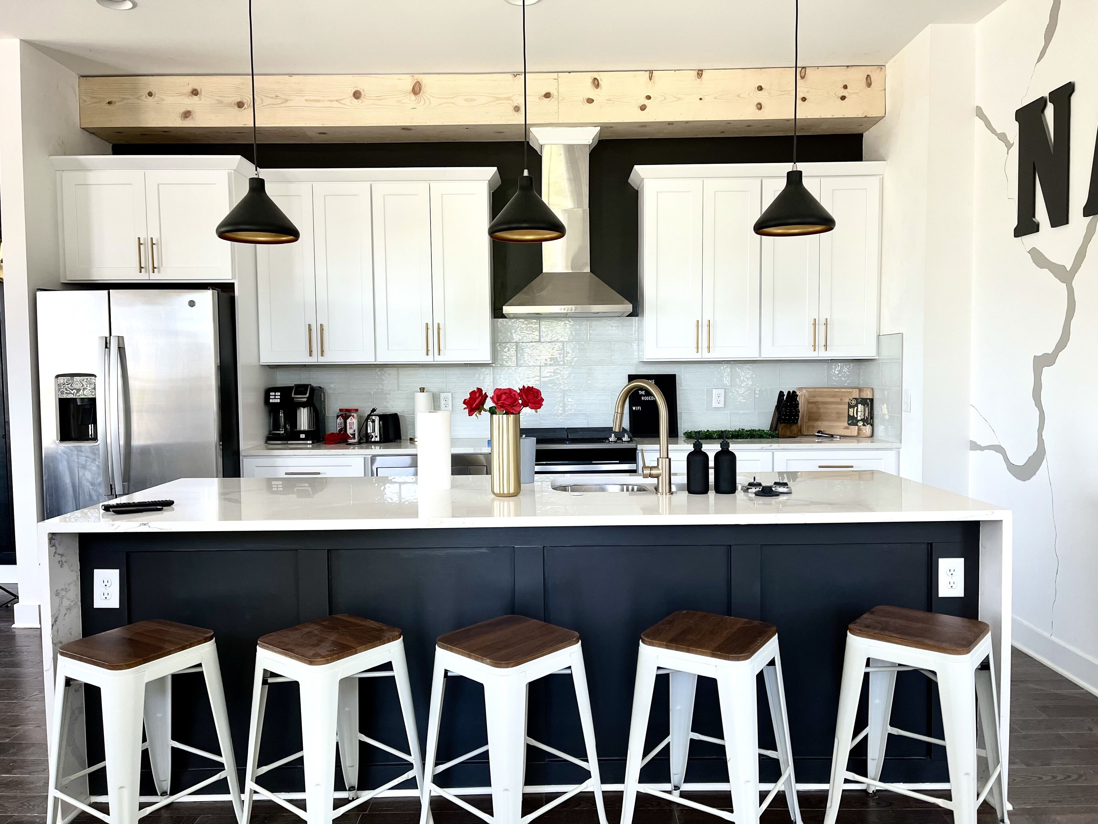 A modern kitchen with white cabinets, a central island with bar stools, pendant lighting, and a stainless steel refrigerator.