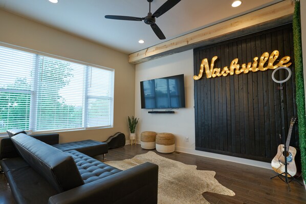 A modern living room with a sectional sofa, a flat-screen TV, a ceiling fan, and a wall-mounted sign that reads "Nashville". - ★Massive Roofdeck★NEW Home-4Bd/3.5Ba- 3miles to downtown (nashville)