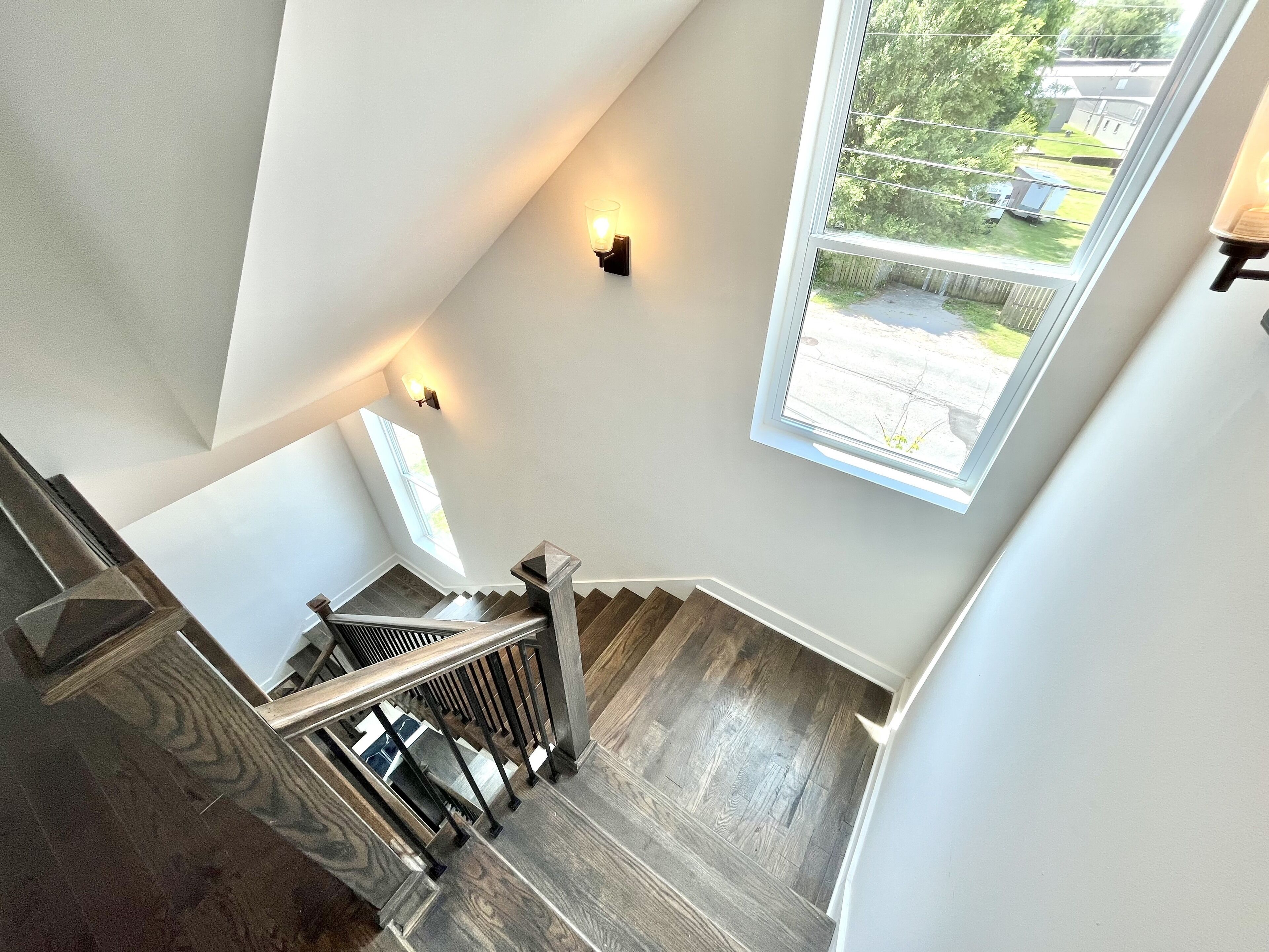 Una scalinata con soffitto alto, gradini in legno e ringhiera in metallo, che conduce a un pianerottolo con vista su un giardino attraverso un'ampia finestra.
