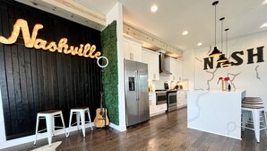 Una cocina moderna con armarios blancos, electrodomésticos de acero inoxidable y una pared de acento negra con letras iluminadas que dicen 'Nashville'.
