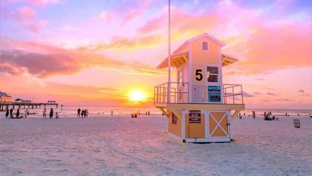 Een strandwachttoren met het getal 5 erop, gelegen op een strand met een ondergaande zon op de achtergrond.