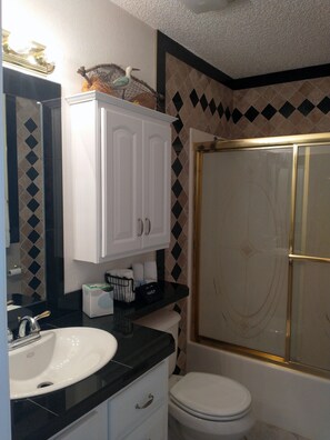 A bathroom with a white sink, black countertop, white cabinets, a white toilet, and a gold-framed shower.