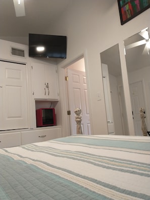 A bedroom with a bed, a TV mounted on the wall, and white cabinets.