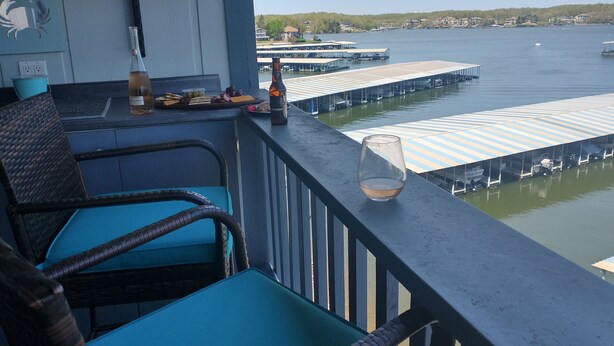 Un balcón con sillones de mimbre, una botella de cerveza y un vaso en la barandilla.