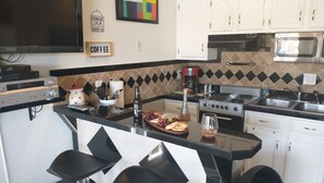 Una cocina con encimera negra, armarios blancos, un microondas, una estufa y un cartel de café.