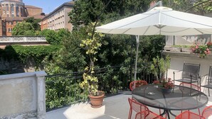 A rooftop terrace with a table and chairs, surrounded by potted plants and a white umbrella.