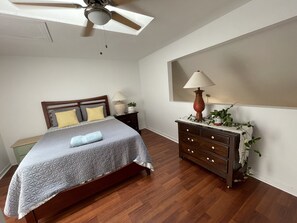 Un dormitorio con cama, cabecero de madera, mesitas de noche, cómoda y ventilador de techo, además de una ventana con vistas.