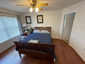 A bedroom with a wooden bed, a ceiling fan, a nightstand with a lamp, and framed pictures on the wall. - Spacious Oversized Townhome! The Blue Water Bungalow (Fort Walton Beach)
