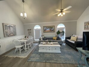 A spacious living room with a dining area, a ceiling fan, and a large window with a view. - Spacious Oversized Townhome! The Blue Water Bungalow (Fort Walton Beach)