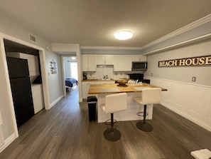 Una cocina moderna con armarios blancos, una isla de madera y un letrero que dice 'BEACH HOUSE'.