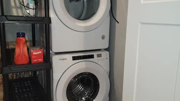 Uma área de lavanderia com duas máquinas de lavar Whirlpool empilhadas, uma cesta e uma embalagem de detergente Bounce.