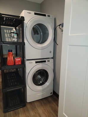 Een wasruimte met twee Whirlpool wasmachines boven elkaar, een mand en een fles Bounce wasverzachter.