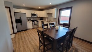 A modern kitchen with white cabinets, stainless steel appliances, and a wooden dining table with chairs. - Completely remodeled downtown apartment!  2 large bedrooms! (Cascade)