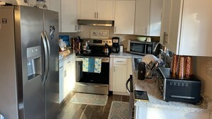 Une cuisine compacte avec des meubles blancs, un réfrigérateur en acier inoxydable, un four à micro-ondes, une cuisinière et une machine à café.
