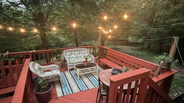 Une terrasse en bois avec des rampes rouges, des meubles en osier et des guirlandes lumineuses.