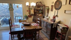Un coin repas accueillant avec une table en bois, des chaises et un tapis à motifs. On peut apercevoir un espace cuisine équipé d’une cuisinière, de placards et de divers ustensiles de cuisine.