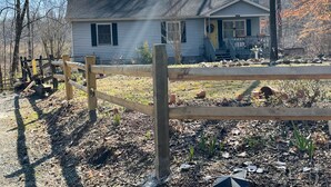 Une maison avec un porche à l’avant, une clôture en bois et une cour avec du paillis et de petites plantes.