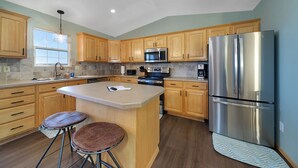Una cocina moderna con armarios de madera, un refrigerador de acero inoxidable, un microondas y una isla grande con taburetes.