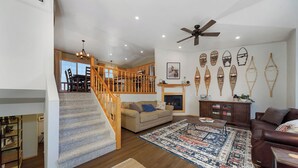 Un salón espacioso con escaleras, chimenea y ventilador de techo.