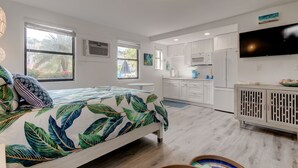 A modern bedroom with a bed, a TV, and a kitchenette in the background. - Poolside Updated Studio Across from the Beach!! (St. Pete Beach)