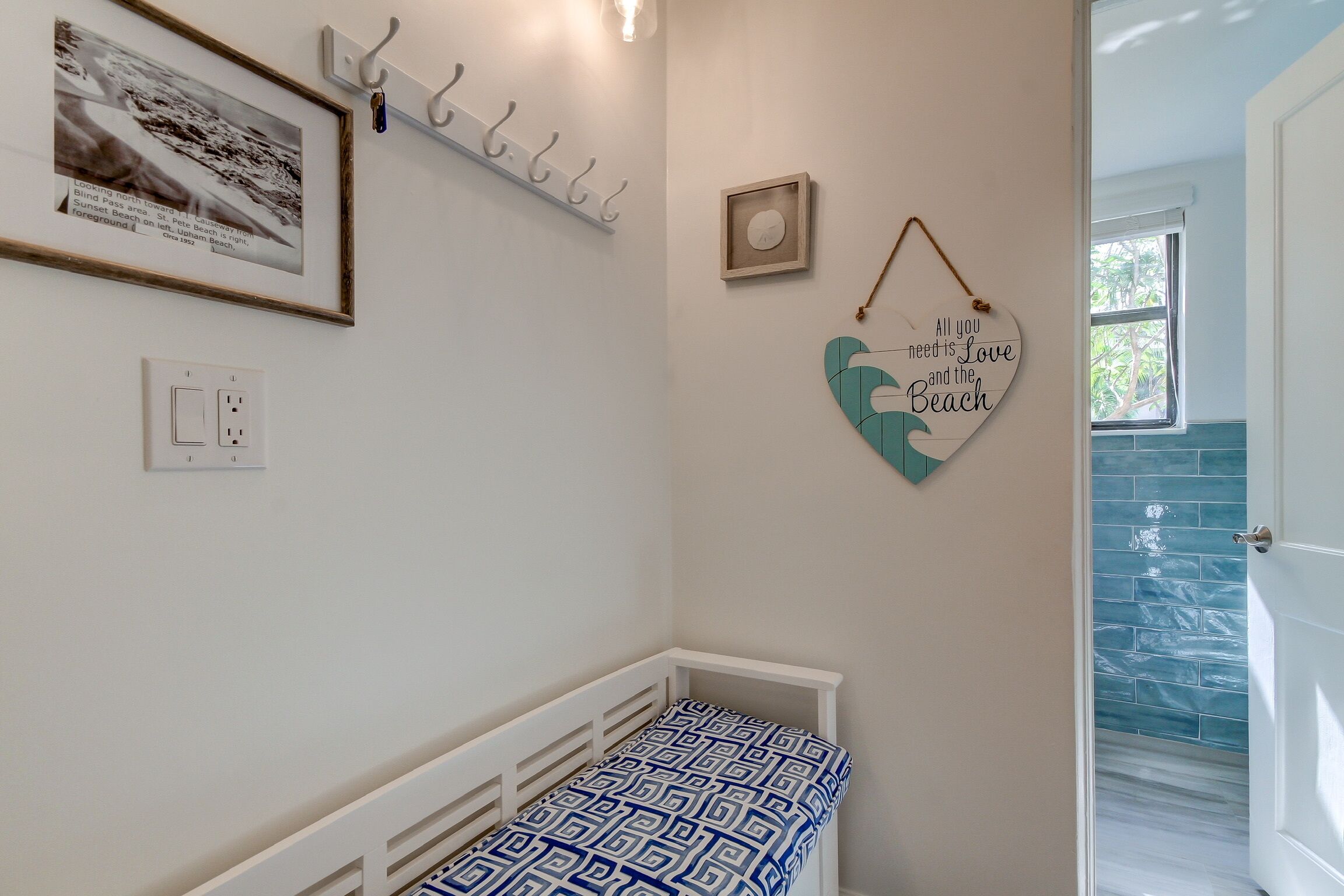 Un dormitorio con una cuna blanca, un retrato enmarcado, un adorno con forma de corazón y una ventana que da a vistas del exterior.