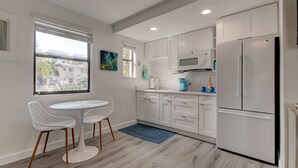 A modern kitchen with white cabinets, a built-in microwave, and a large refrigerator. There is a dining area with two white chairs and a small table. - Poolside Updated Studio Across from the Beach!! (St. Pete Beach)