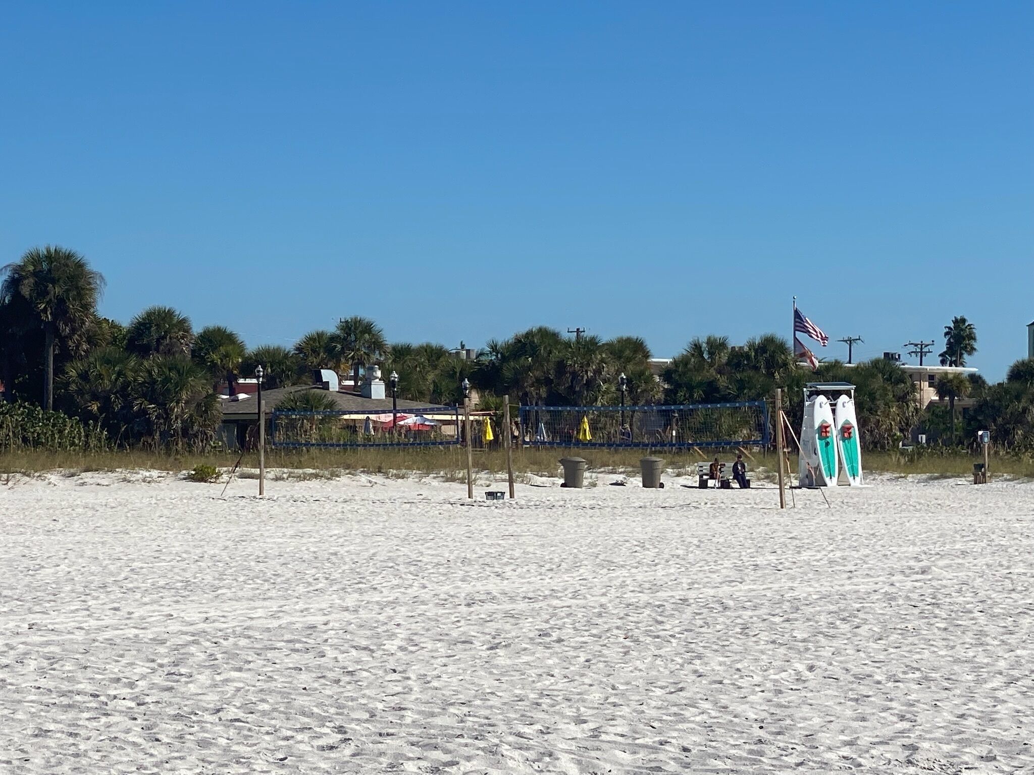 A beach with a fence, beach chairs, and surfboards.