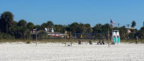 A beach with a fence, beach chairs, and surfboards.