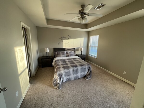 A bedroom with a bed, nightstands, a ceiling fan, and a window with blinds.
